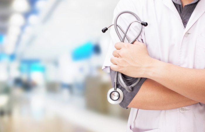 Una persona con bata blanca está de pie, con los brazos cruzados y un estetoscopio en la mano, encarnando la presencia autoritaria de un profesional médico que aparece en el Boletín Médico. El entorno difuminado del hospital o la clínica refuerza el enfoque en la experiencia de EuroEspes Health.