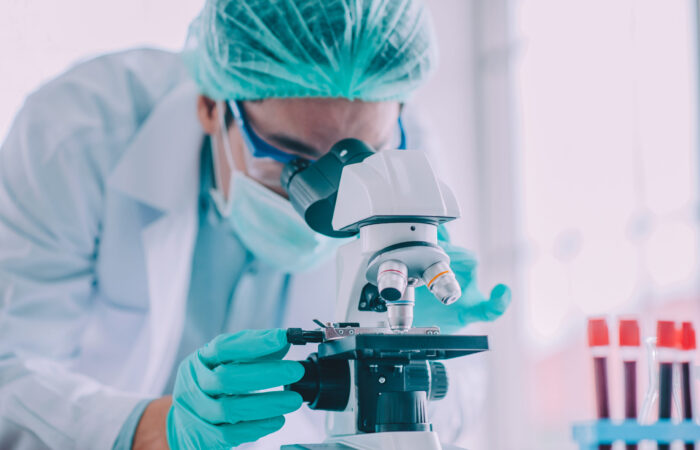 En medio de una cascada de tubos de ensayo que contienen un líquido rojo vibrante, un científico con bata de laboratorio, mascarilla verde y redecilla para el pelo observa a través de un microscopio. Los guantes azules garantizan un manejo cuidadoso mientras realizan meticulosamente una investigación para la publicación de salud Boletín Médico EuroEspes. En medio de una cascada de tubos de ensayo que contienen un líquido rojo vibrante, un científico con bata de laboratorio, mascarilla verde y redecilla para el pelo observa a través de un microscopio. Los guantes azules garantizan un manejo cuidadoso mientras realizan meticulosamente una investigación para la publicación de salud Boletín Médico EuroEspes.